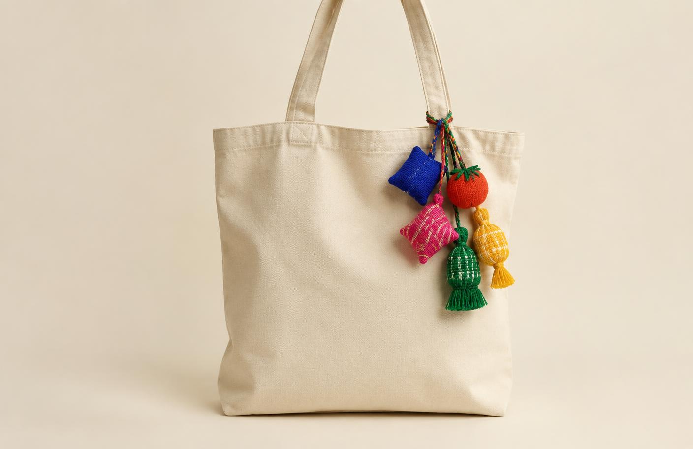 Five woven charms in bright colours hanging off a cotton tote, mid-swing.